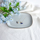 Origami butterfly earrings on a decorative plate with flowers on a light background