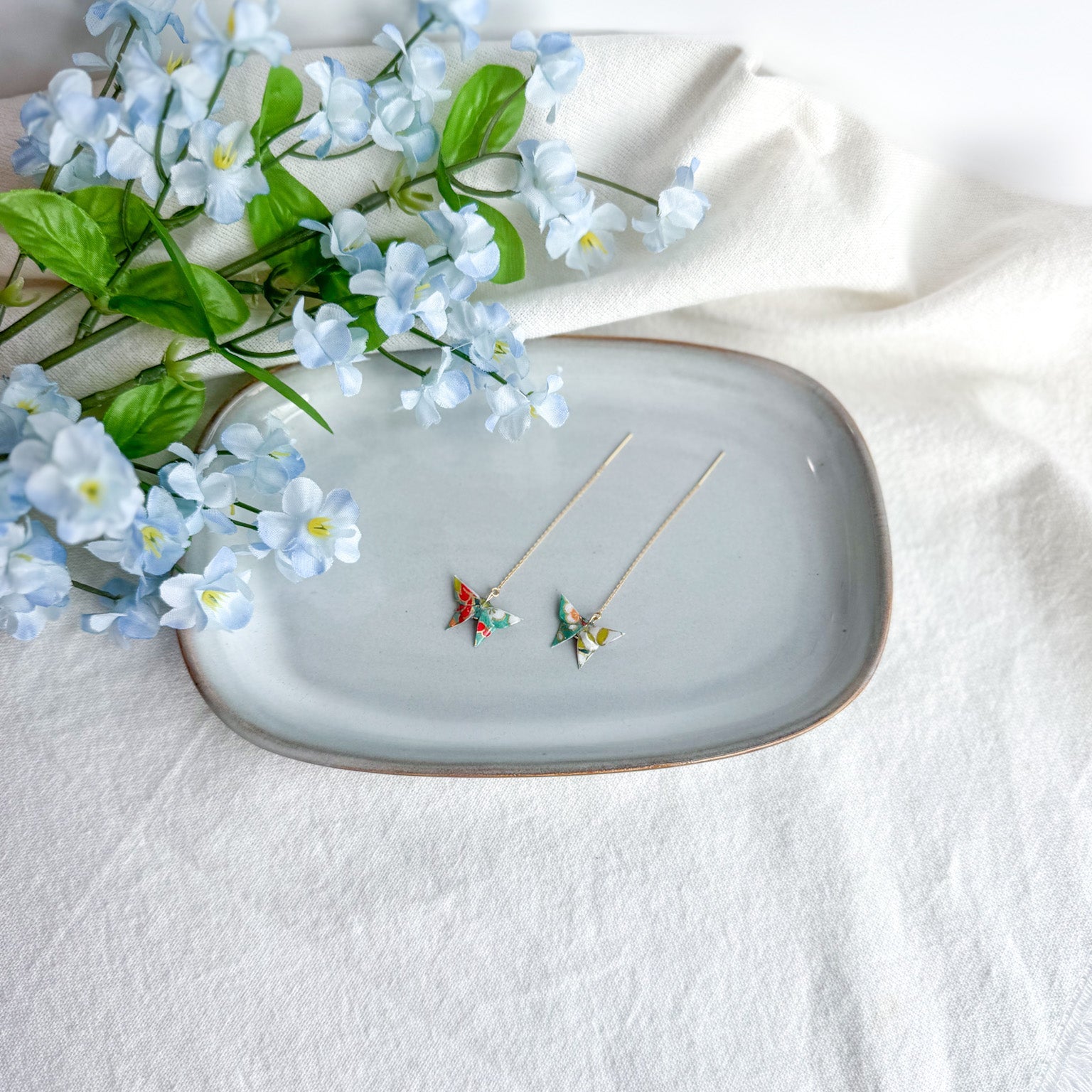 Origami butterfly earrings on a decorative plate with flowers on a light background