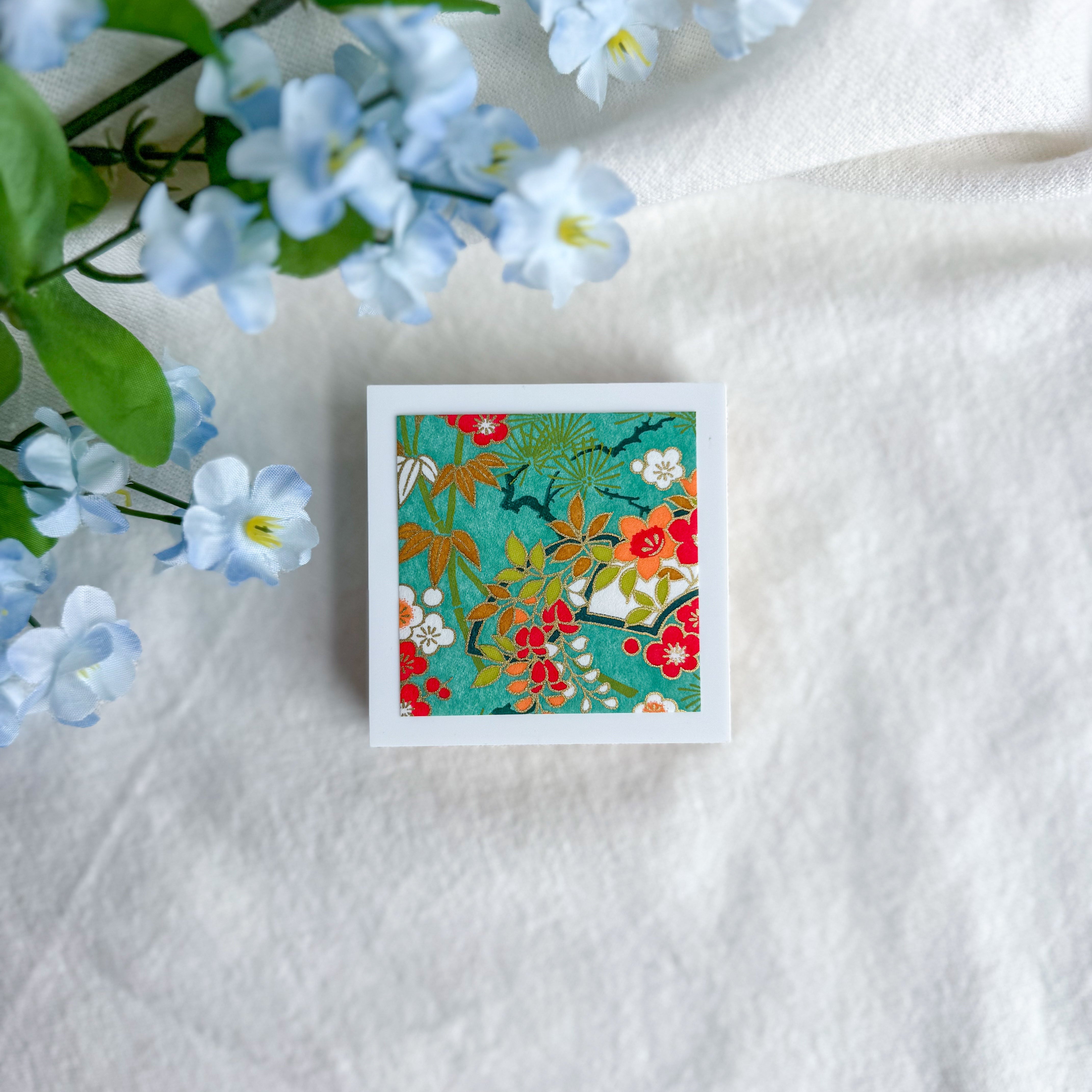 Green floral design washi paper on a white fabric background with blue flowers.