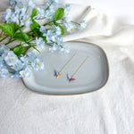 Origami butterfly earrings on a decorative plate with flowers on a light background