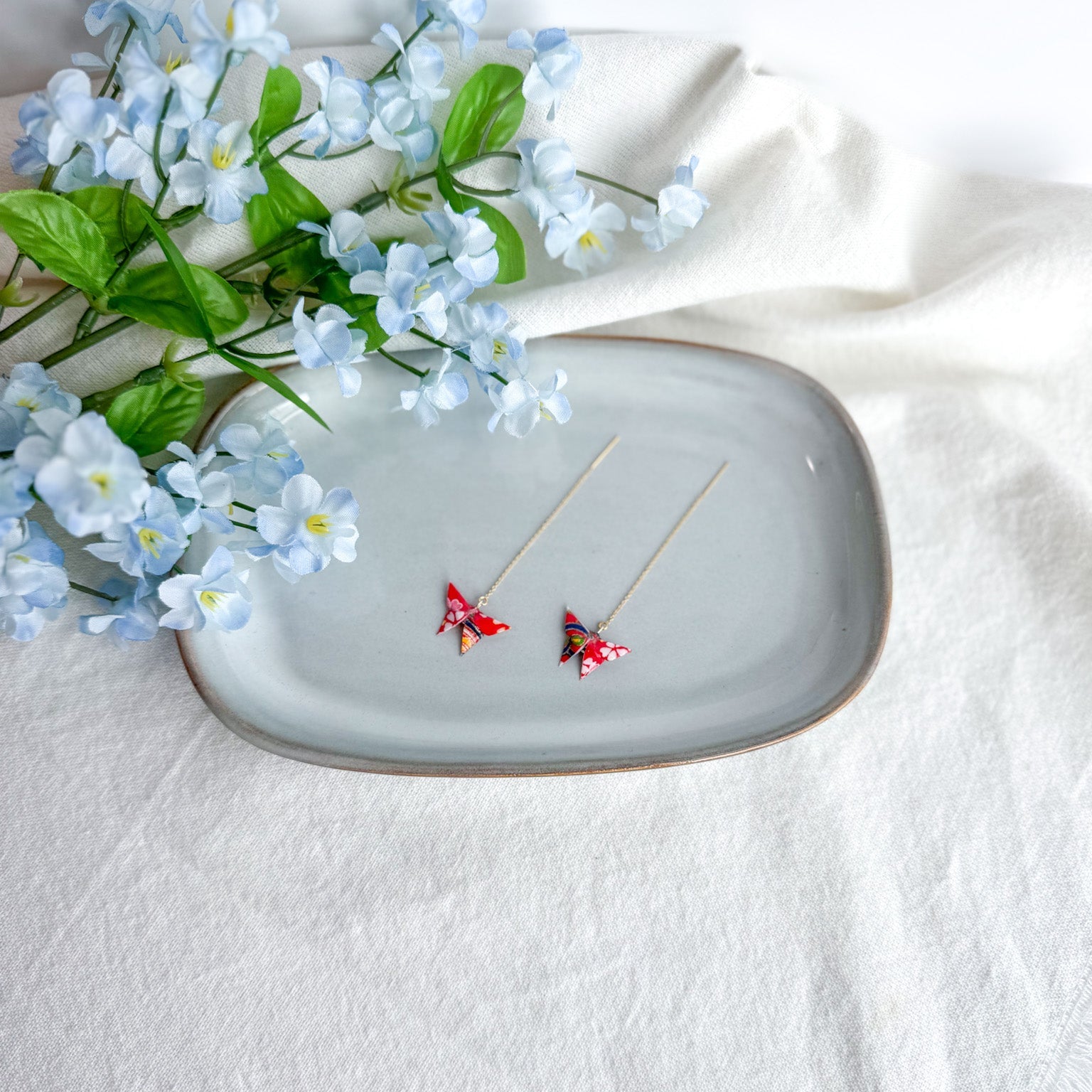 Origami butterfly earrings on a decorative plate with flowers on a light background