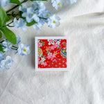 Red floral design washi paper on a white fabric background with blue flowers.
