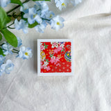 Red floral design washi paper on a white fabric background with blue flowers.