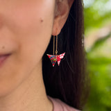 Close-up of a person wearing colorful origami butterfly earrings with a blurred green background