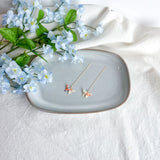 Origami butterfly earrings on a decorative plate with flowers on a light background