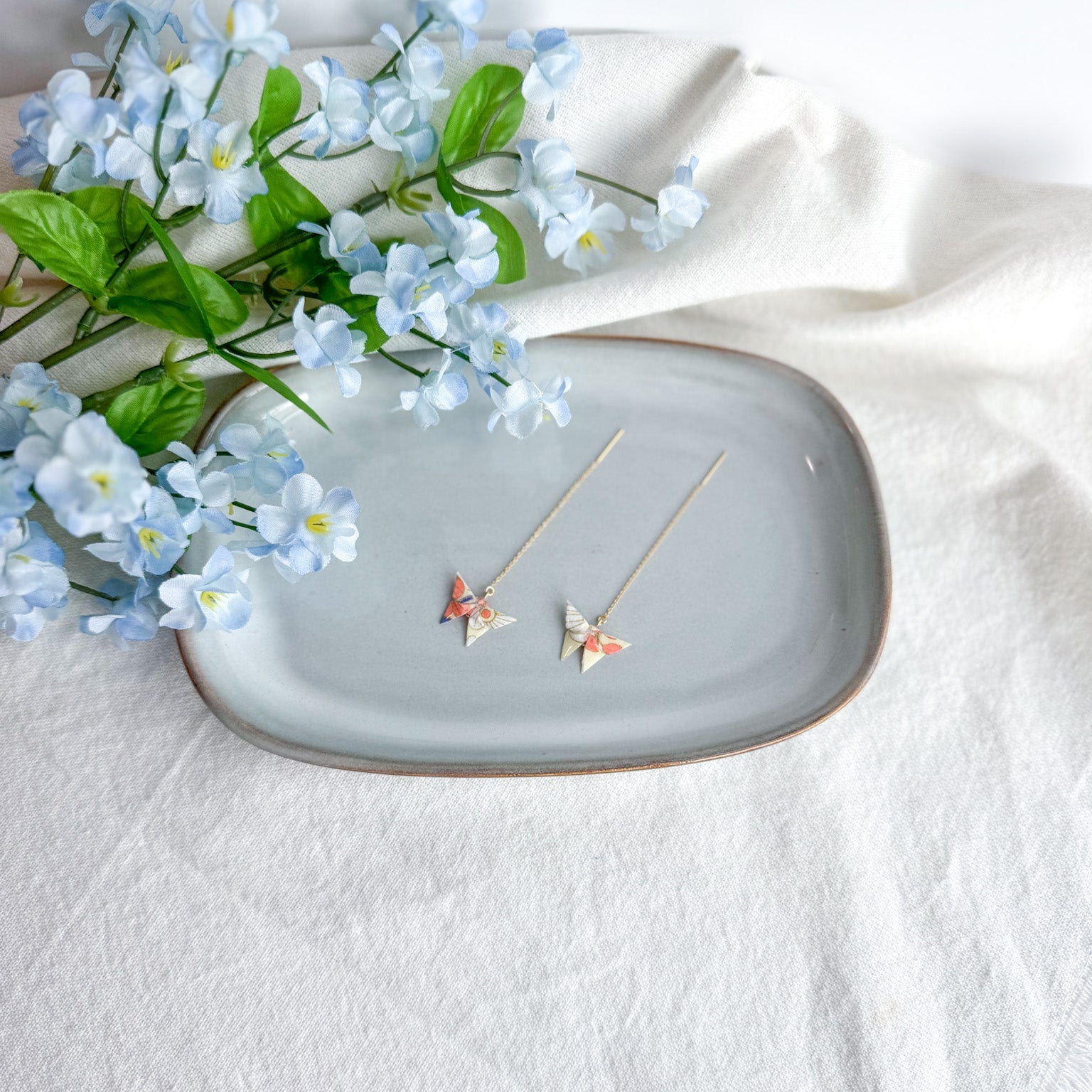 Origami butterfly earrings on a decorative plate with flowers on a light background