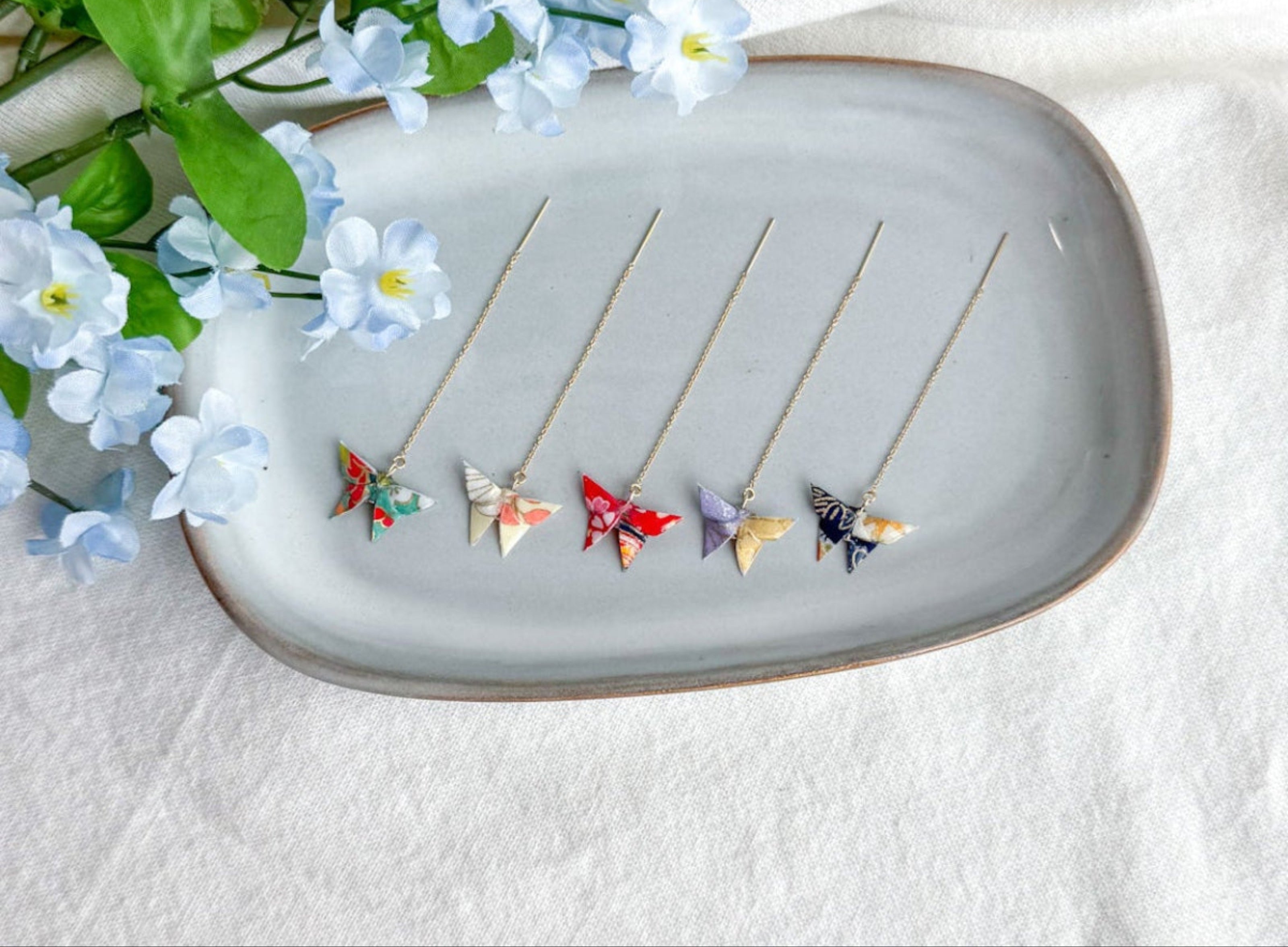 Tray with origami butterfly earrings on a white fabric background