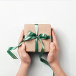 Hands holding a small gift box with a green ribbon on a white background