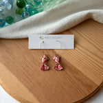 Pair of pink origami koi fish earrings on a wooden surface with a white branded card