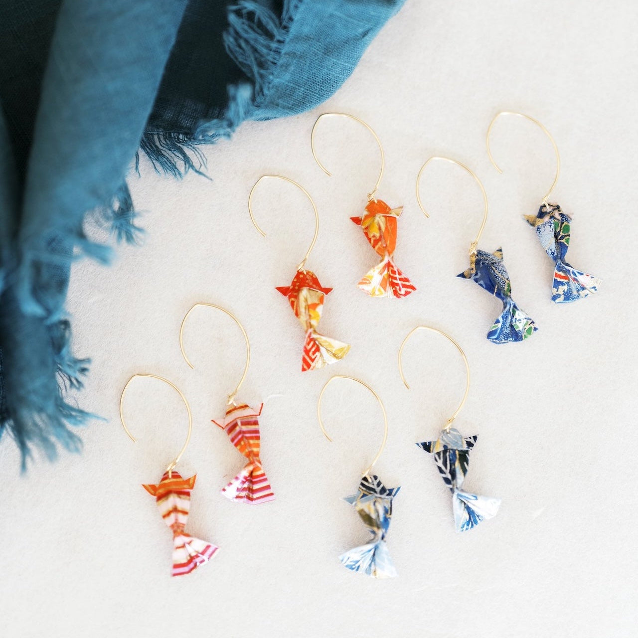 Colorful koi fish-shaped origami earrings on a white surface with a blue scarf.