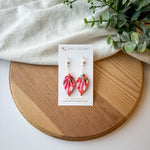 Colorful origami leaf earrings on a card with a wooden board and white fabric background