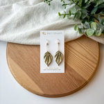 Colorful origami leaf earrings on a card with a wooden board and white fabric background