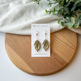 Colorful origami leaf earrings on a card with a wooden board and white fabric background