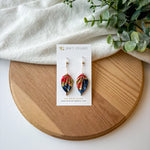 Colorful origami leaf earrings on a card with a wooden board and white fabric background