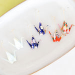 Colorful origami crane earrings on a plate with a lime and white background