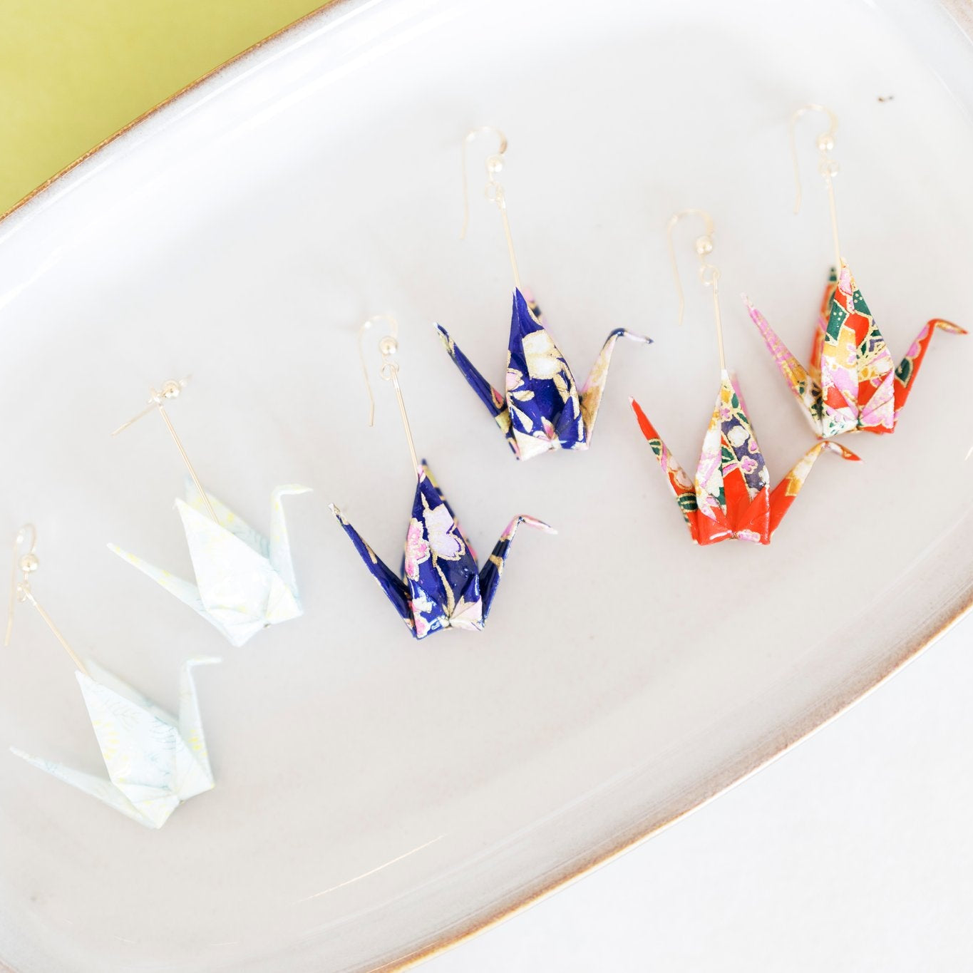 Colorful origami crane earrings on a plate with a lime and white background