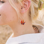 A person wearing a pair of origami crane earrings made of Japanese washi paper and 14K gold-filled findings.