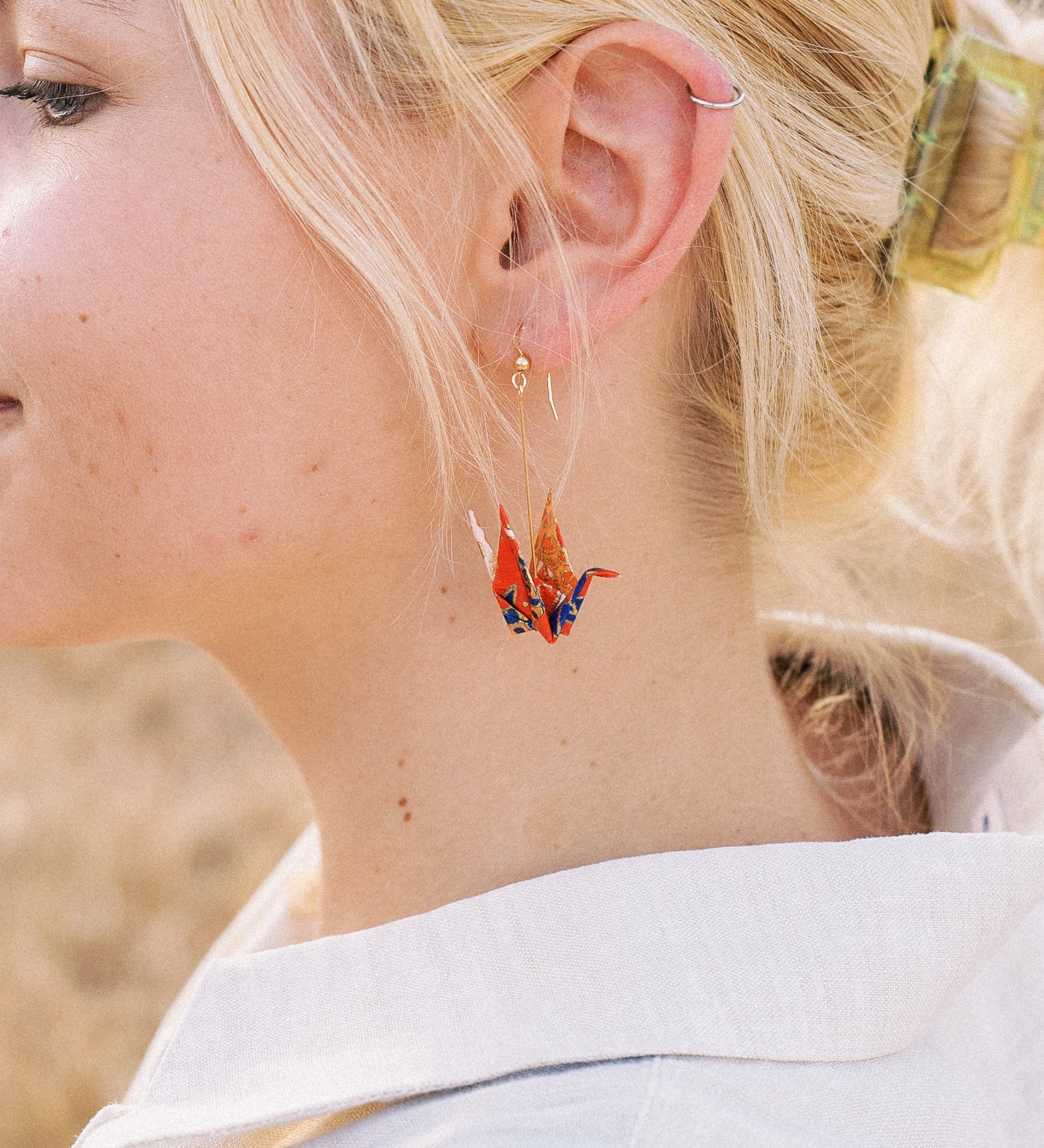 A person wearing a pair of origami crane earrings made of Japanese washi paper and 14K gold-filled findings.