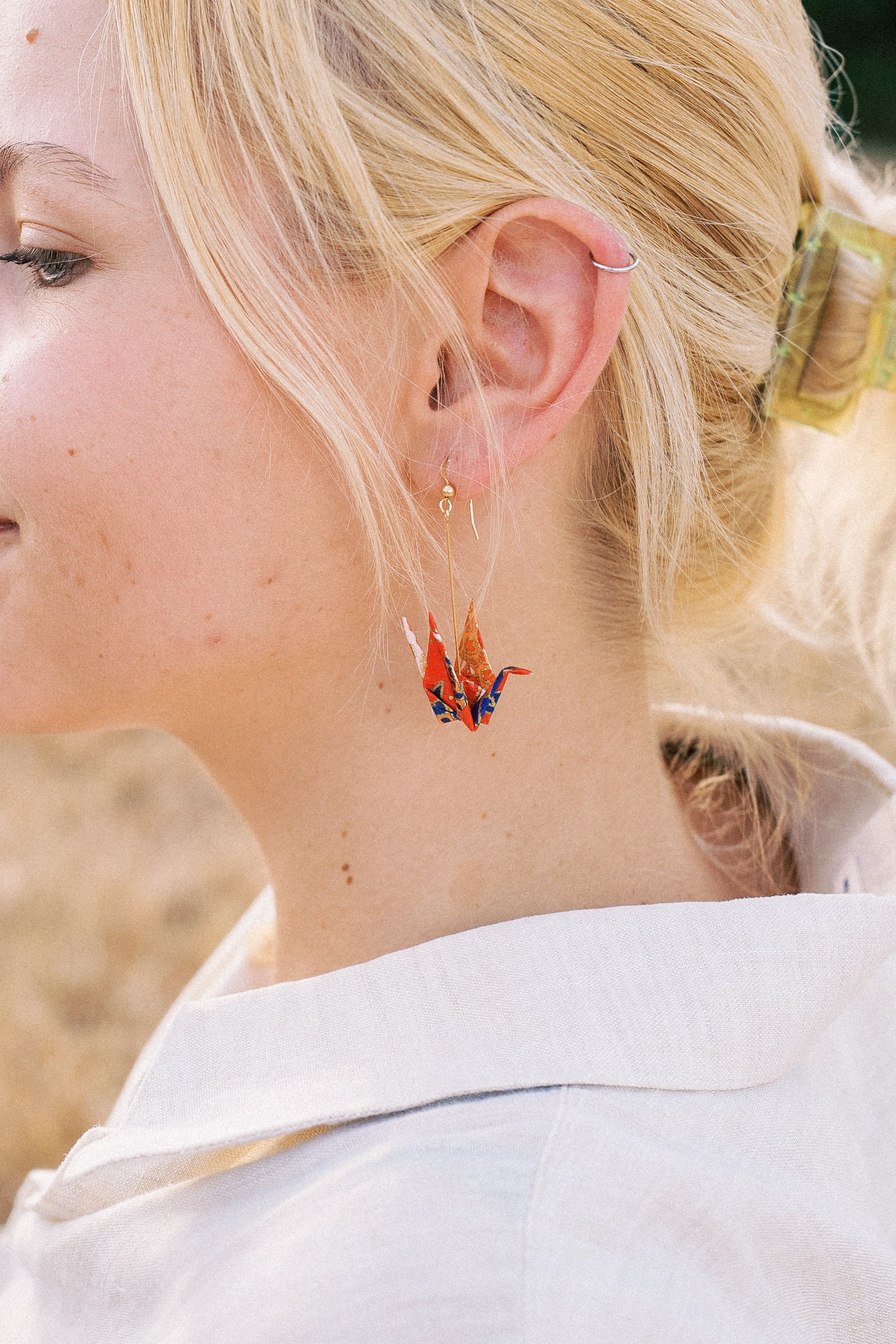 A person wearing a pair of origami crane earrings made of Japanese washi paper and 14K gold-filled findings.