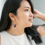 A person with dark hair wearing a pair of origami crane earrings made of Japanese washi paper and 14K gold-filled findings.