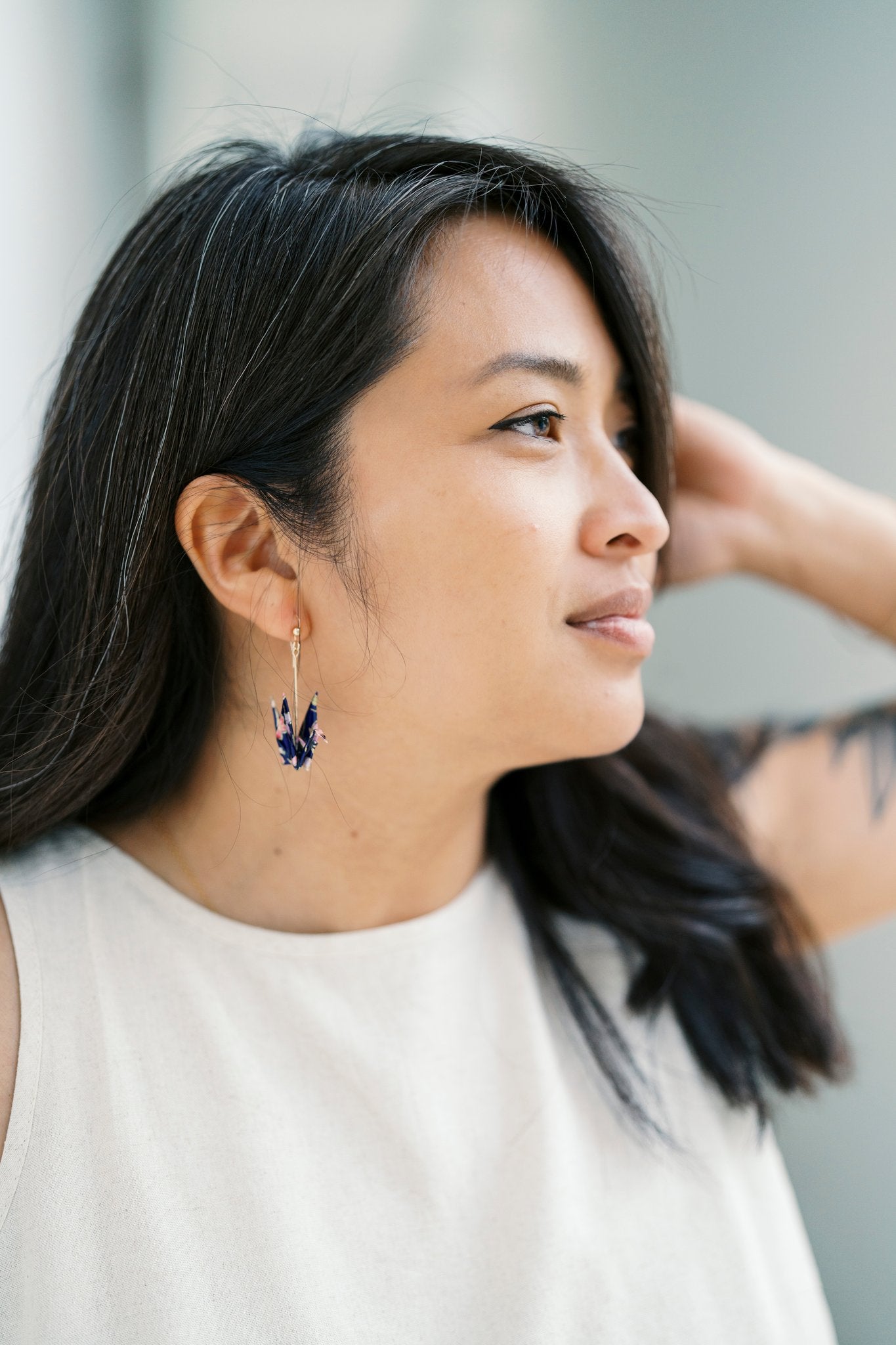 A person with dark hair wearing a pair of origami crane earrings made of Japanese washi paper and 14K gold-filled findings.