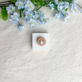 Round origami crane magnet on a white square surface next to blue flowers