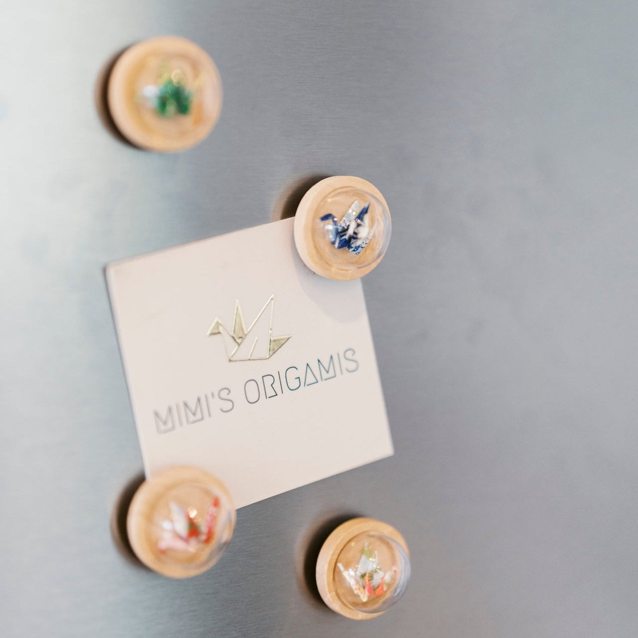 Mimi's Origamis business card on a refrigerator with wooden origami crane magnets.