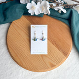 Origami crane earrings on a wooden surface with white flowers and green fabric