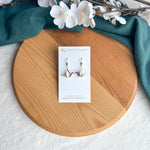 Origami crane earrings on a wooden surface with white flowers and green fabric