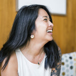 Woman wearing earrings and necklace laughing, with a blurred background