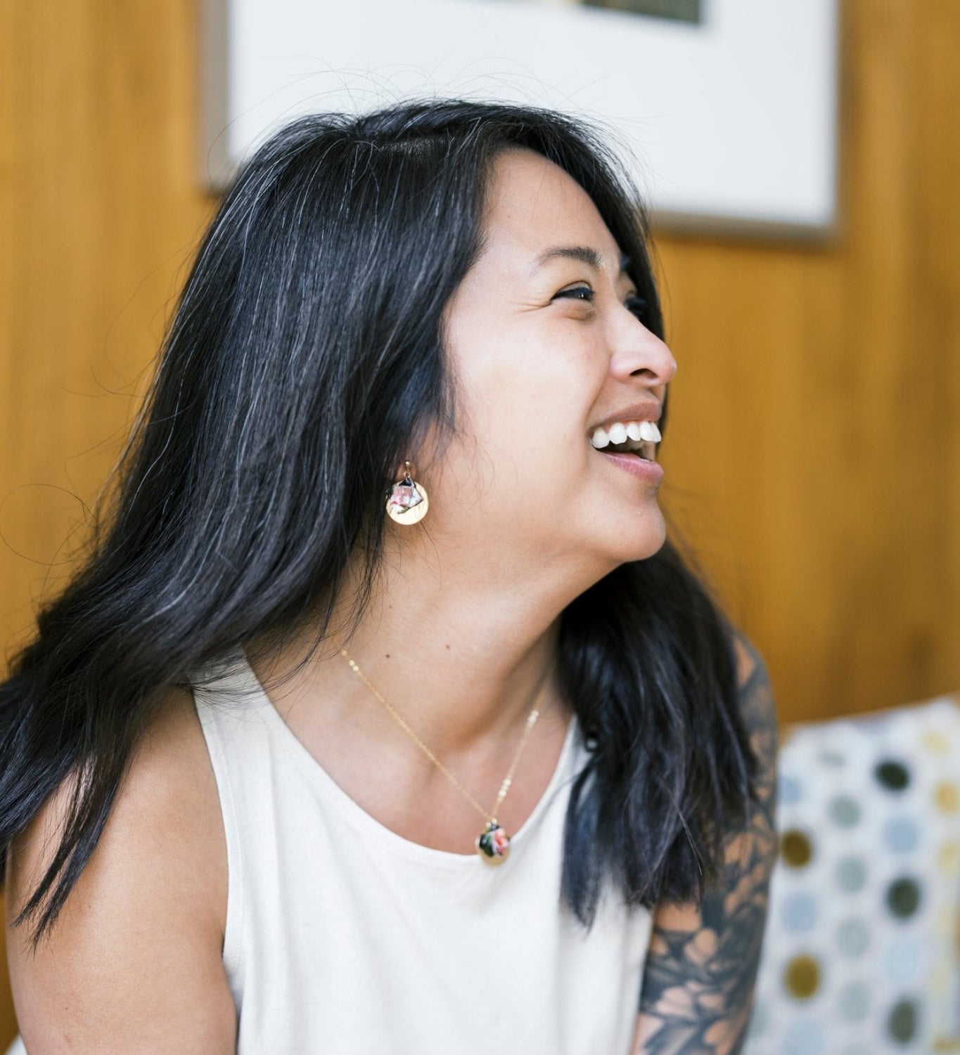Woman wearing earrings and necklace laughing, with a blurred background