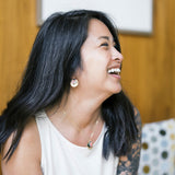 Woman wearing earrings and necklace laughing, with a blurred background