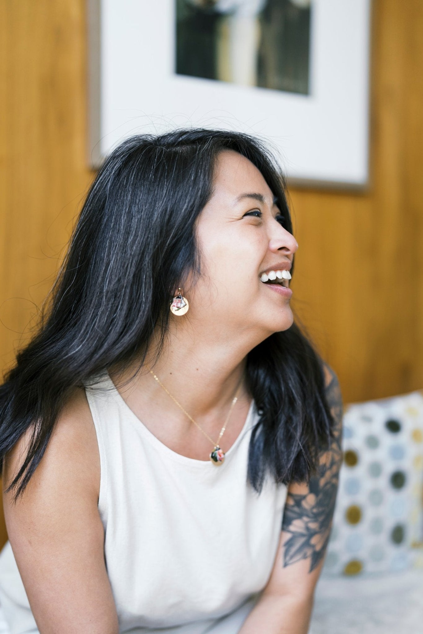 Woman wearing earrings and necklace laughing, with a blurred background