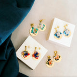 Colorful origami earrings on white stands with a wood and fabric background