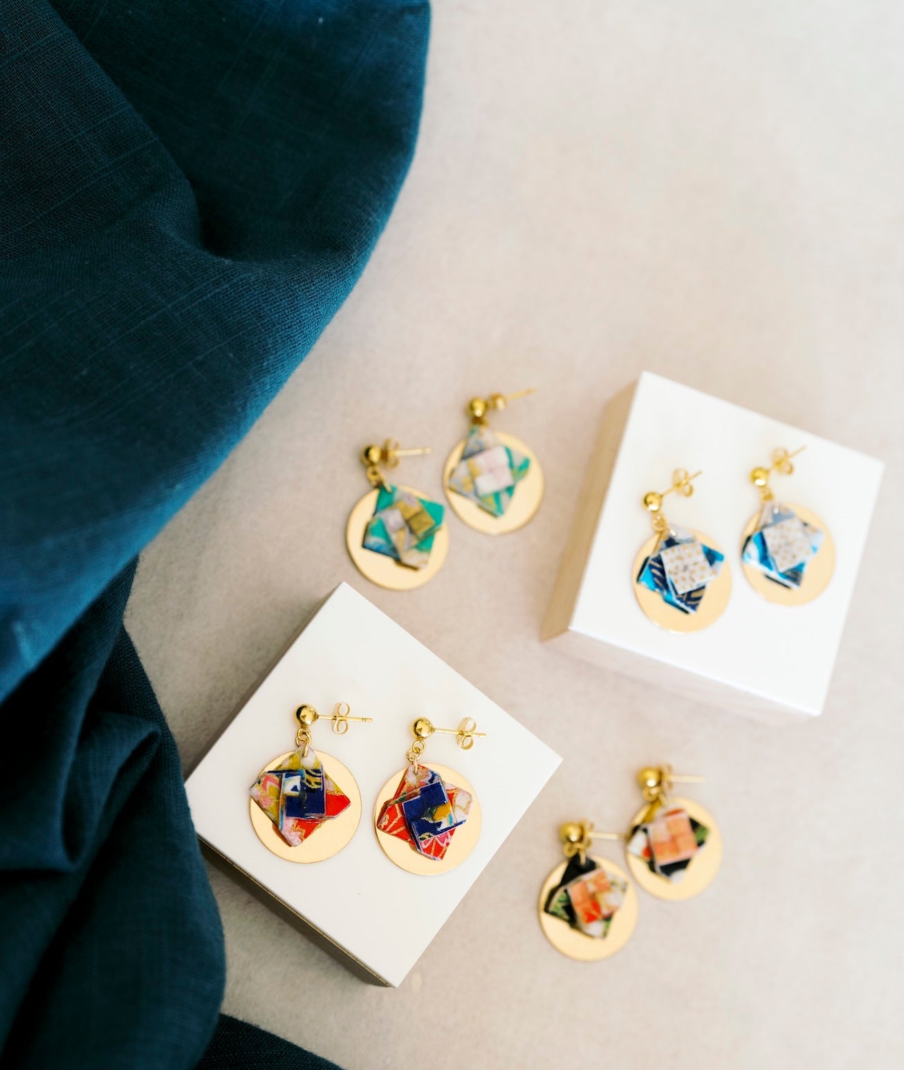 Colorful origami earrings on white stands with a wood and fabric background