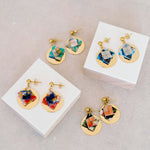 Colorful origami earrings on white blocks with a fabric background