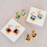 Colorful origami earrings on white blocks with a fabric background