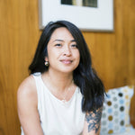 Woman wearing matching earring and necklace sitting on a bench with a wooden wall and framed picture in the background
