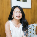 Woman wearing matching earring and necklace sitting on a bench with a wooden wall and framed picture in the background