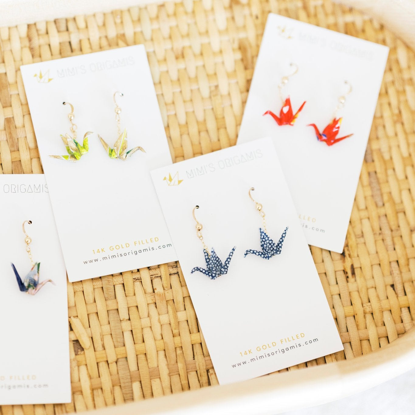 Set of tiny origami crane earrings on cards  on a woven tray