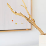 A set of delicate gold-tone bezel bracelets, hanging from a decorative driftwood branch stand in a white pot against a bright, softly blurred background.