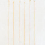 Six delicate gold chain necklaces with small, colorful circular pendants are arranged vertically in a row on a clean white background.